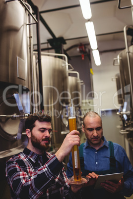 Worker and owner inspecting beer at brewery