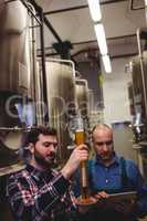 Worker and owner inspecting beer at brewery