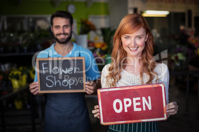 Woman holding open signboard and man holding slate with flower shop sign
