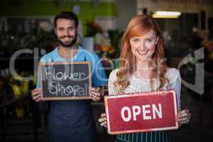 Woman holding open signboard and man holding slate with flower shop sign