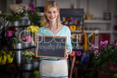 Smiling female florist holding open sign on slate in flower shop
