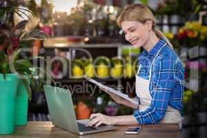 Female florist using laptop while holding clipboard