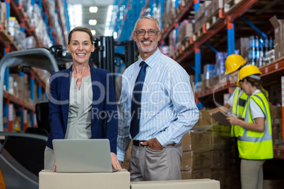 Portrait of warehouse manager and client standing with laptop