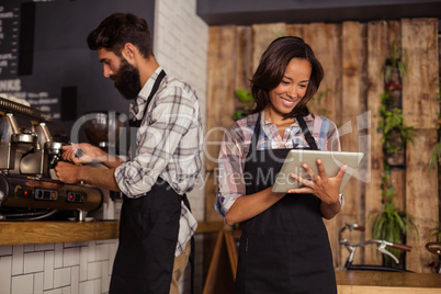 Waitress using digital tablet while waiter preparing coffee in background