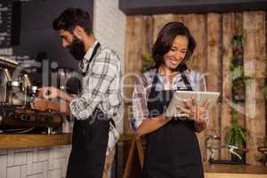Waitress using digital tablet while waiter preparing coffee in background