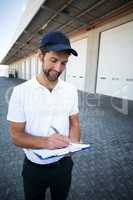 Smiling delivery man writing on clipboard