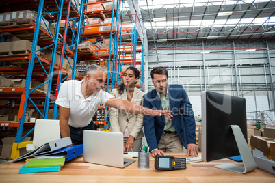 Warehouse managers and worker discussing with computer