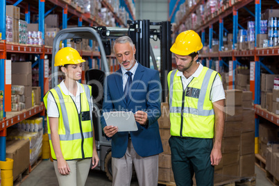 Warehouse manager and co-workers discussing over clipboard