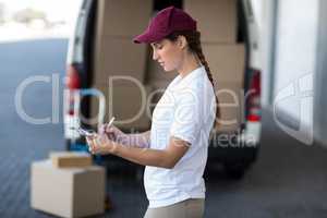 Delivery woman writing on clipboard while standing next to van