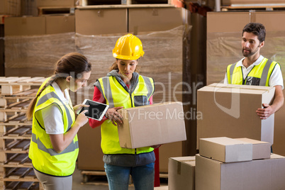 Manager noting on digital tablet while workers carrying cardboard boxes