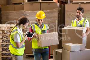 Manager noting on digital tablet while workers carrying cardboard boxes