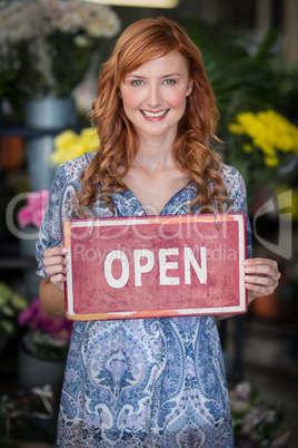 Smiling florists holding open sign placard in flower shop