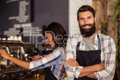 Portrait of waiter standing with arms crossed while waitress working in background