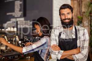 Portrait of waiter standing with arms crossed while waitress working in background