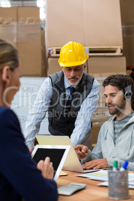 Warehouse manager and staff discussing with laptop