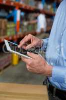 Mid section of warehouse worker using digital tablet