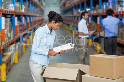 Female warehouse worker with a clipboard checking the boxes