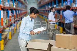 Female warehouse worker with a clipboard checking the boxes
