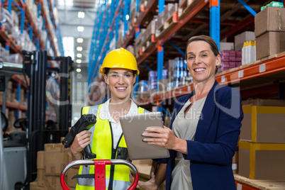 Warehouse manager and female worker smiling while holding digital tablet