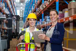 Warehouse manager and female worker smiling while holding digital tablet