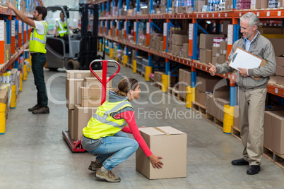 Warehouse manager showing thumbs up to female worker while carrying cardboard boxes