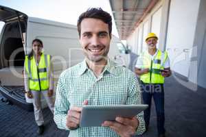 Portrait of manager using digital tablet and workers standing in background