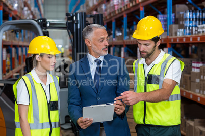 Warehouse manager and co-workers discussing over clipboard