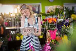 Female florist talking on mobile phone and using digital tablet