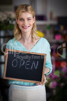 Smiling female florist holding open sign on slate in flower shop