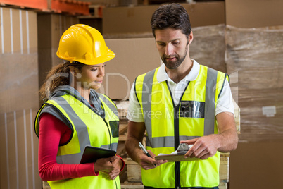 Warehouse workers discussing with clipboard and digital tablet