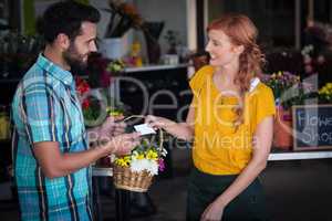 Female florist giving visiting card and flower basket to customer