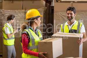 Smiling warehouse workers carrying a cardboard box