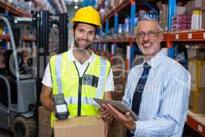 Warehouse manager holding digital tablet while male worker scanning barcode