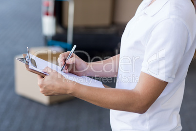 Mid section of delivery woman writing on clipboard