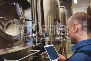 Male manufacturer using digital tablet by machinery