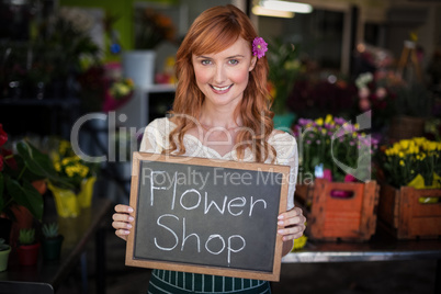 Portrait of female florist holding slate with flower shop sign