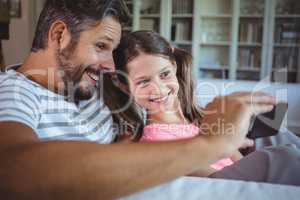 Smiling father and daughter looking at mobile phone in living room