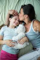 Mother kissing on daughter forehead on bed
