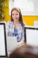 Portrait of beautiful executive with headphones using laptop at creative office