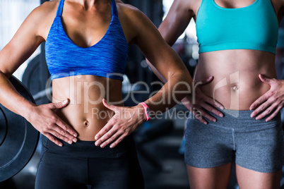 Midsection of female friends touching belly in gym