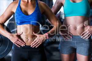 Midsection of female friends touching belly in gym