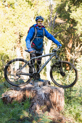 Male mountain biker standing on tree stump with bicycle