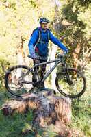 Male mountain biker standing on tree stump with bicycle
