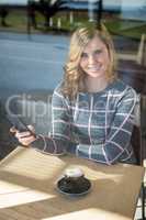Woman using mobile phone while having cup of coffee