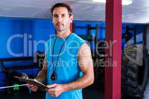 Serious instructor holding clipboard in gym