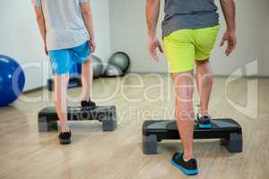 Two men doing step aerobic exercise with dumbbell on stepper