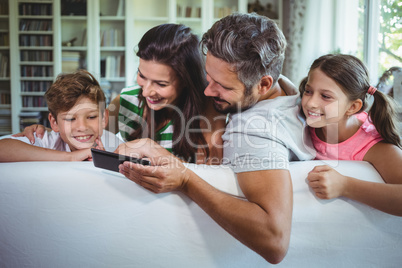 Parents sitting on sofa with their children and using mobile phone in living room