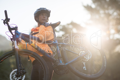 Female biker carrying mountain bike and walking