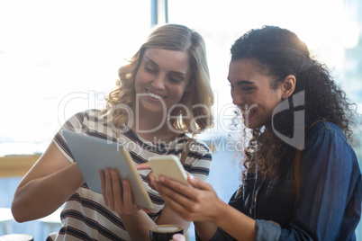 Women using mobile phone and digital tablet in cafÃ?Â©