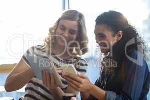 Women using mobile phone and digital tablet in cafÃ?Â©